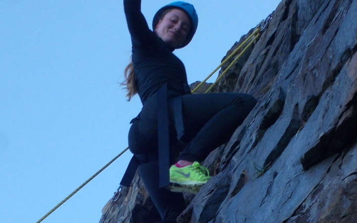 a rock climber raises a hand and smiles as they navigate a rock wall